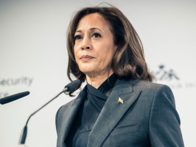 Vice President. Kamala Harris wears a serious expression as she stands before a pair of microphones