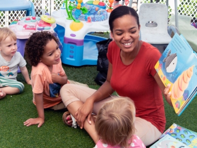 image of teacher holding up a book, reading to children