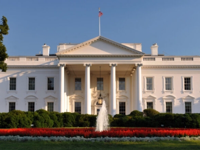 The north entrace to the White House, in late-day sunlight, with a garden and fountain in the foreground and a deep blue sky in the background
