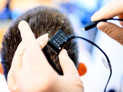Closeup of gloved hands connecting a brain-computer-interface to the back of research participant's head.