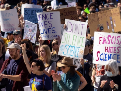 protesters in a crowd with signs reading Science Saves Lives, Don't Silence Science and Fascism Hates Science