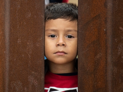 a young child looking through two bars of the wall between the US and Mexico
