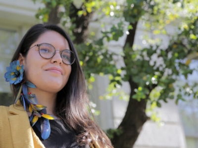 a woman with dark hair and glasses wearing a blue and yellow feathered earring