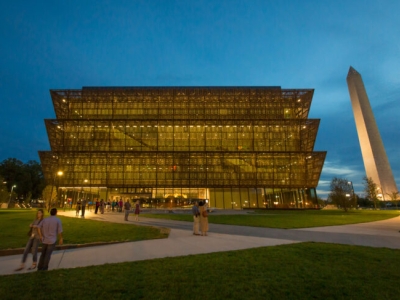 a multistory museum with a brown lattice exterior pictured at night, with a white obelisk rising in the background.