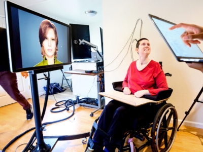 Ann Johnson sits in her wheelchair with a cord plugged into a neuroprosthesis implant while she participates in a clinical trial helping to restore her ability to speak with a brain-computer interface