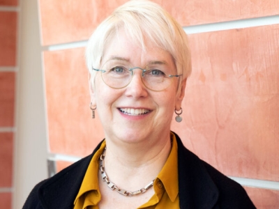 smiling woman with white hair and glasses wearing a mustard blouse with black jacket