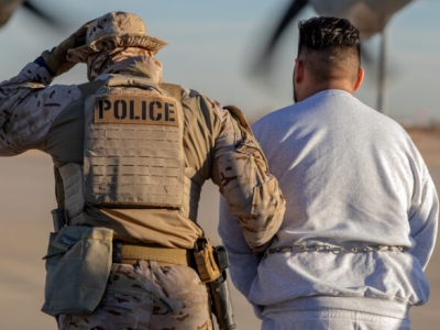 A photo showing from behind a person in military fatigues and a sidearm in a holster, with a 