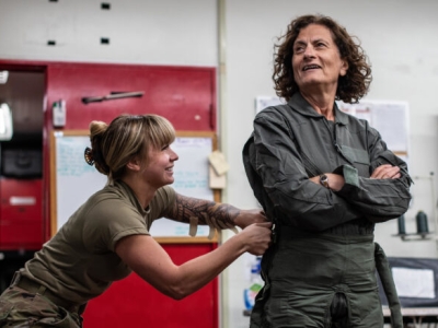 a young woman cinches up the green flight suit of an older woman