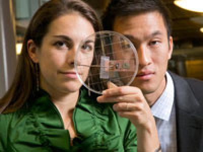 Two people standing with glass disk raised in front of their faces.