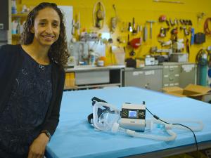 Associate professor Grace O'Connell stands next to a ventilator, which is lying on a table in her lab, that she created from a used sleep apnea machine