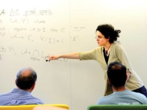 woman discussing math in front of whiteboard, two men looking on