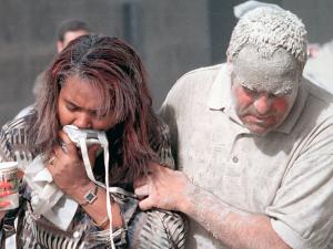 a woman with her face covered against fumes is supported by an ash-covered man near the site of the World Trade Center collapse