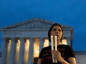 a solemn protester with two candles stands before the US Supreme Court building as darkness falls