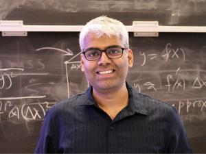 Picture of Gopala Anumanchipalli standing in front of a chalk board with formulas chalked on it.  