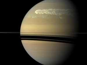 closeup of beige planet with stormy swirls at top and shadow of rings at middle