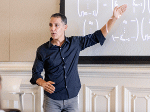 UC Berkeley professor Hany Farid stands at the front of a classroom, gesturing at equations projected onto a large screen 