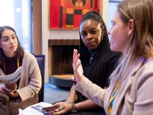 two women, left and center, listen to a third woman at right who is talking and gesturing