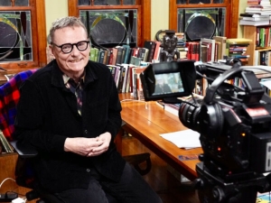 Economist James A. Robinson, sitted at a desk in a happily cluttered office, smiling as he waits to start a video interview