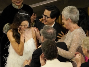 Michelle Yeoh stands with a hand to her mouth as Jamie Lee Curtis and Ke Huy Quan congratulate her.