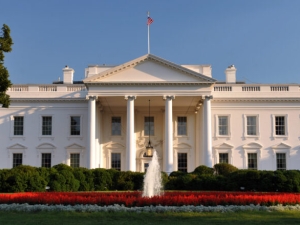 The north entrace to the White House, in late-day sunlight, with a garden and fountain in the foreground and a deep blue sky in the background
