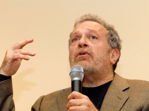 Robert Reich with microphone and gesticulating as though talking