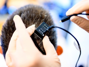 Closeup of gloved hands connecting a brain-computer-interface to the back of research participant's head.