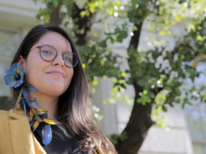 a woman with dark hair and glasses wearing a blue and yellow feathered earring