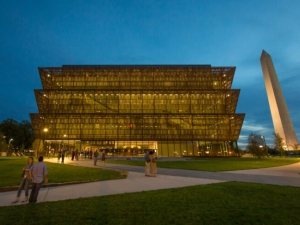 a multistory museum with a brown lattice exterior pictured at night, with a white obelisk rising in the background.