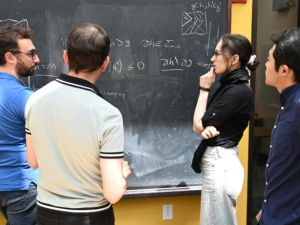 three men and a woman staring at a blackboard as one person explains the figures on the board