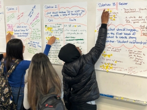 Students point toward poster paper on the wall during an exercise about the ways to better understand chronic absenteeism among students.