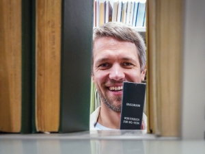 Gasper Begus looks at the camera smiling from behind a bookshelf