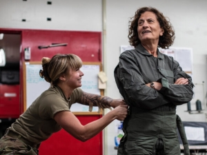 a young woman cinches up the green flight suit of an older woman