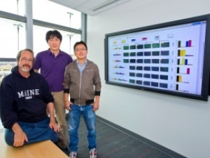 3 people standing next to a wall-mounted screen