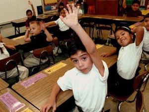 children in classroom; one holding their hand up