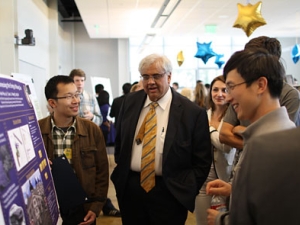 Sastry standing with others in front of a poster 