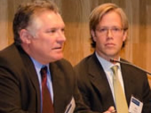 2 people sitting on panel; one talking the other listening
