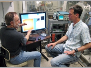 2 men site in front of a computer screen in a lab.