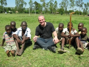 man sitting in grassy field with young people near him