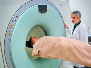 Man standing next to person entering a CT scanner 