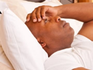 man lying in bed awake with hand over forehead