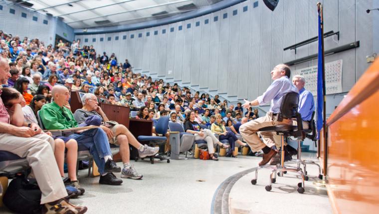 Nobel Laureate Saul Perlmutter speaking in front of full auditorium.